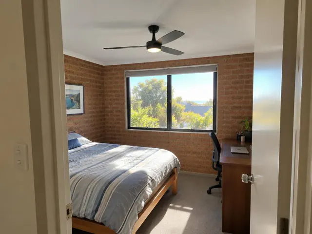 Ceiling fan in a brick-walled bedroom with bed, desk and window in Terrigal