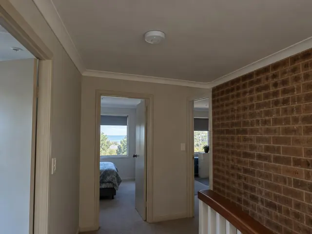 Hallway ceiling smoke alarm in a beige home interior with brick feature wall in Forresters Beach